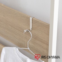 頂天立地木質收納架的側邊，金屬掛鉤懸掛著一件白色衣物。收納架板材為淺木紋色，搭配白色直立支架。