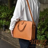 職人手作皮革三層收納兩用商務公事包，採用天然皮革製作，呈現溫潤的焦糖棕色。包款設計簡潔，擁有雙提把及可拆卸肩帶，方便手提或肩背。包身結構分明，可容納多樣物品，適合商務或日常使用。