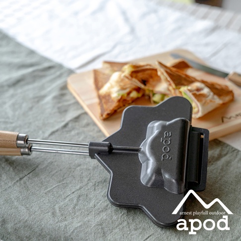 黑色金屬熱壓三明治烤夾，帶有木質手柄，烤夾上印有「apod」字樣，旁邊擺放著切成三角形的烤三明治。