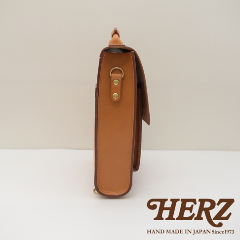 皮革復古後背包，側邊視角，呈現原色皮革材質，配有金色 D 形環和鉚釘。