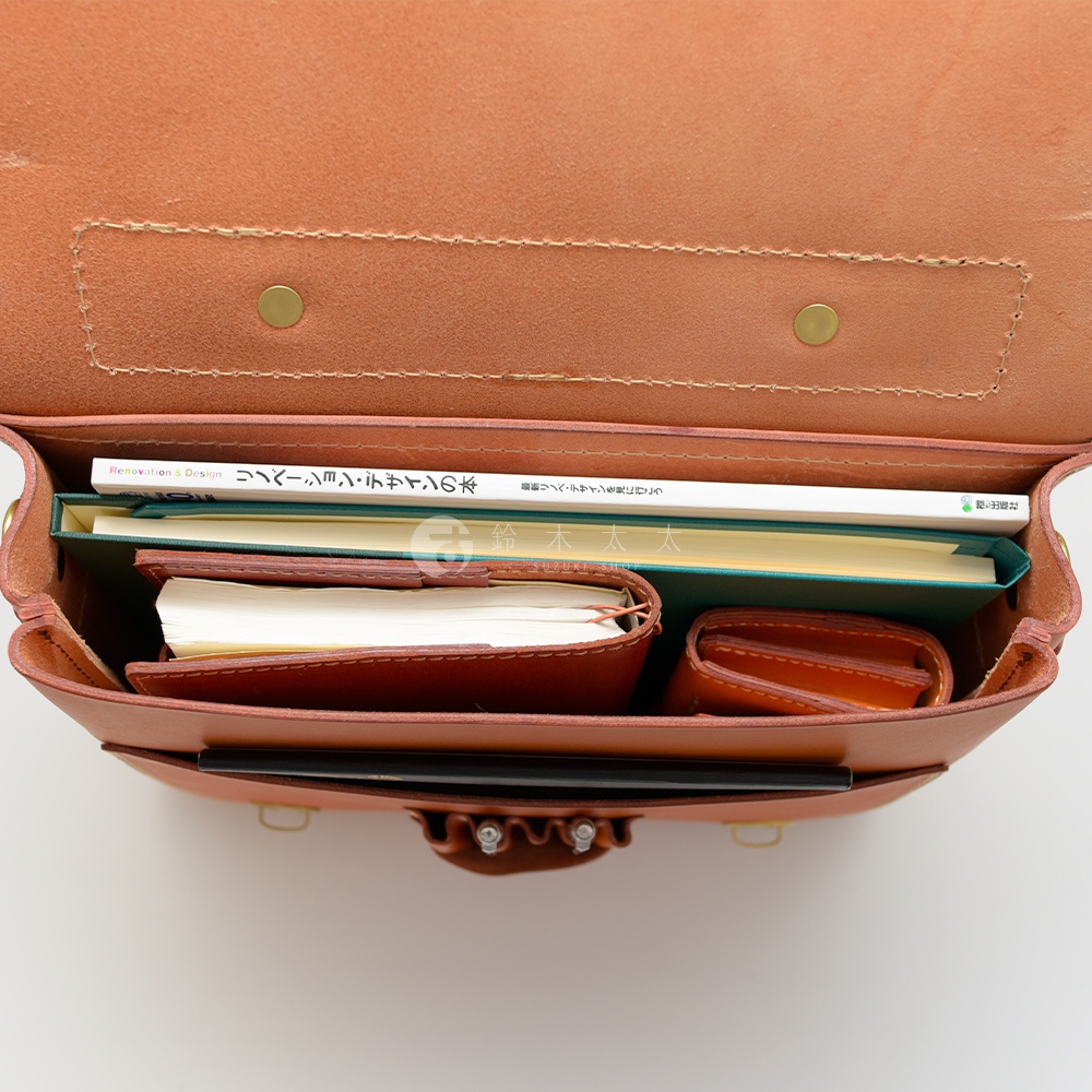 職人手作皮革歐風三用學生包，展示內部空間，裝有書本、筆記本和錢包，包身為淺棕色皮革。