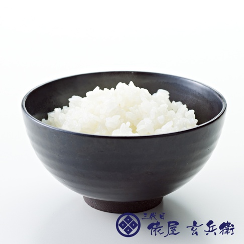 黑色陶瓷碗中盛有飽滿的白色米飯，碗底有深色材質，碗邊緣有細微紋理。