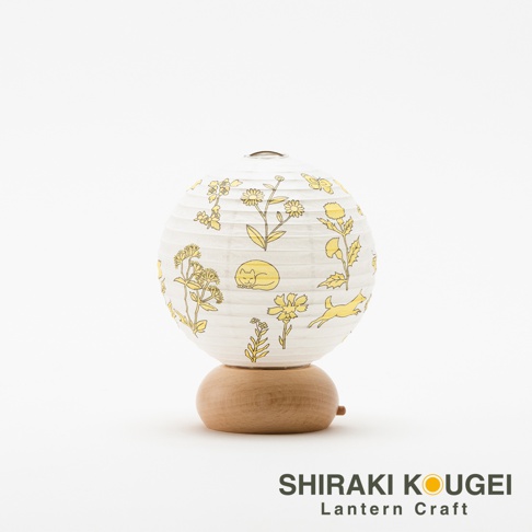 白色紙質圓形提燈，印有黃色線條繪製的植物、蝴蝶、睡貓和奔跑的動物圖案，燈身由木紋圓形底座支撐。