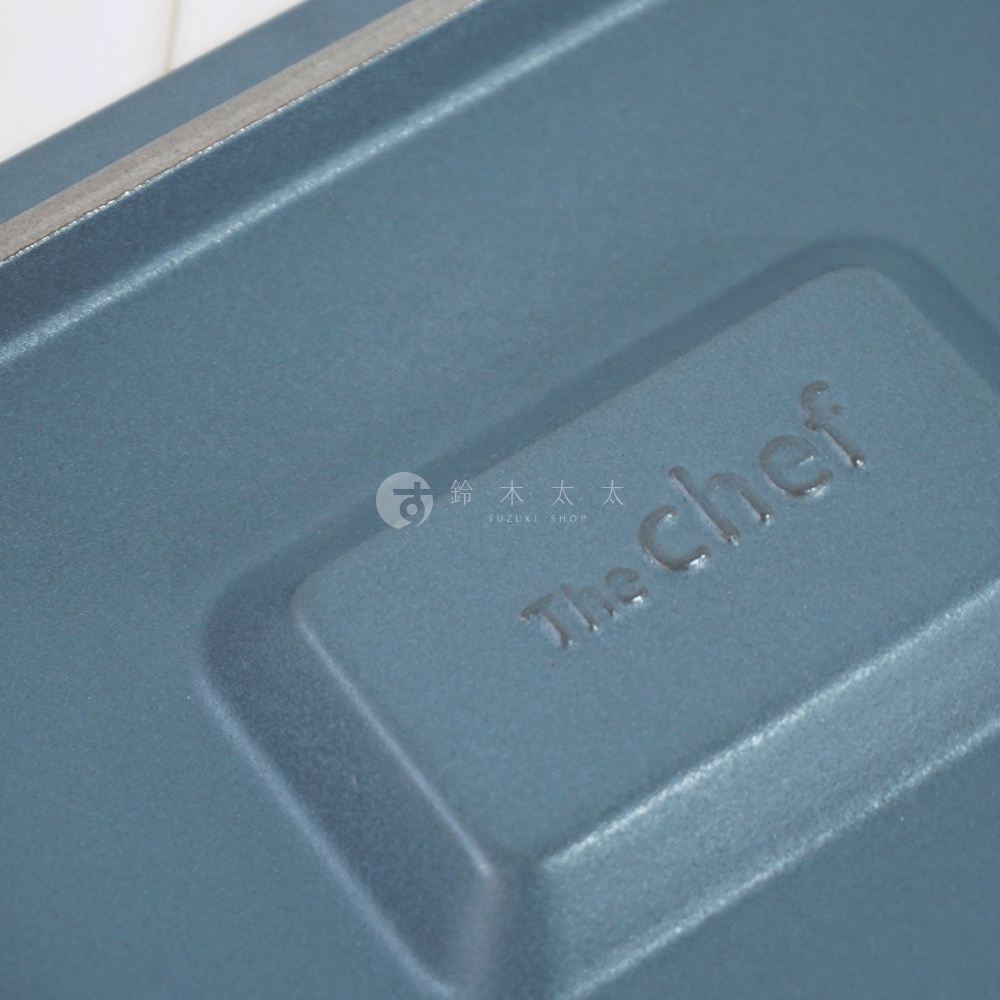 藍灰色陶製烤盤，表面壓印有「The Chef」品牌標誌，材質為耐熱陶，呈現平底設計，適合烹飪用途。