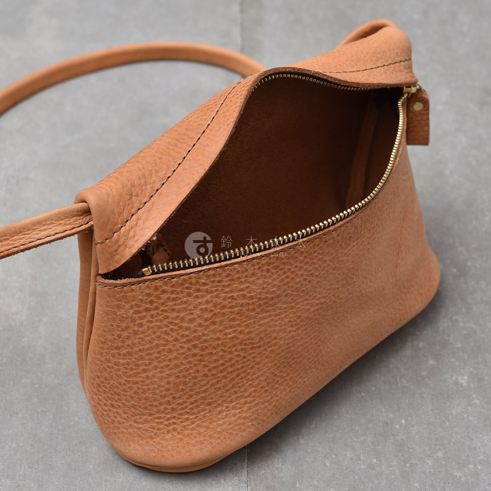 一個棕褐色的皮革斜背包，帶有拉鍊開口，展示其內部。