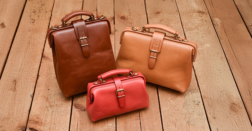 職人手作皮革迷你軟皮杜勒斯包，展示紅、棕、淺棕三色。包款為復古醫生包造型，採用真皮材質，配有黃銅釦具及單手提把，展現精緻工藝。