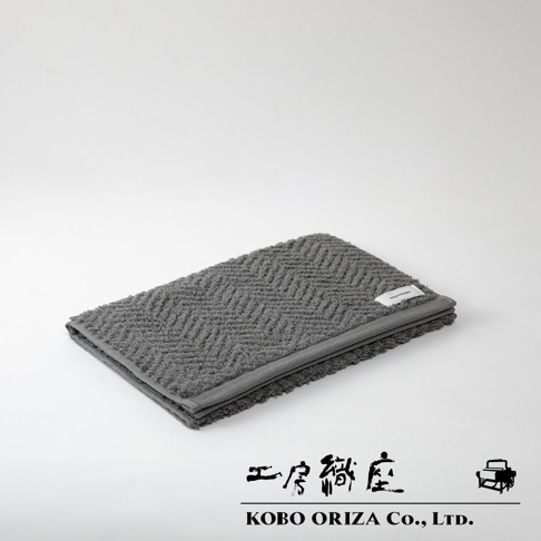 ECOR 天然系人字紋有機棉毛巾，深灰色，材質為柔軟的有機棉，織有清晰的人字紋路，邊緣有同色系滾邊，右上角有白色品牌標籤。