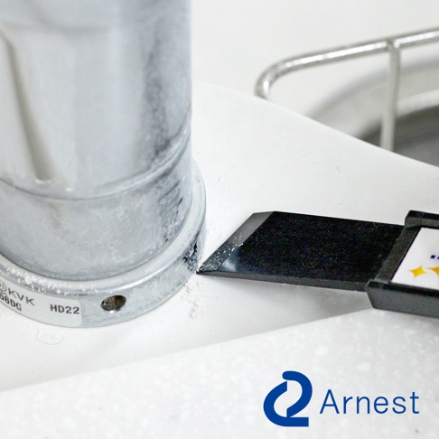 一個銀色金屬圓柱體旁，一個黑色刮刀的尖端正刮除白色表面的污垢。