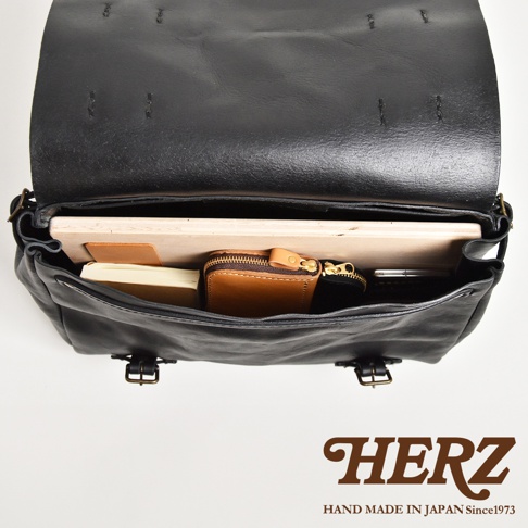 職人手作皮革復古郵差包，黑色，內部可見一個棕色皮夾、一本筆記本和一個平板電腦。