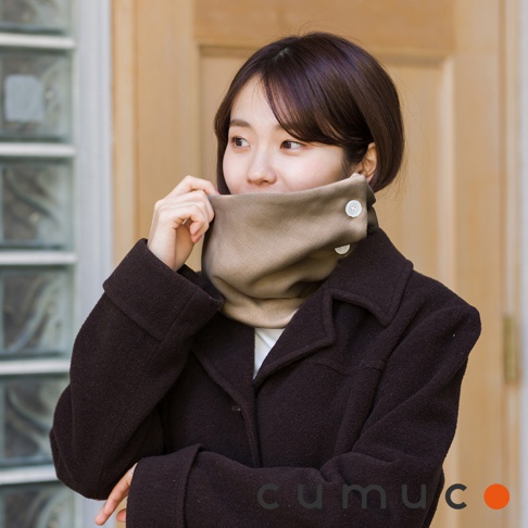 一位女士戴著米色圍脖，穿著深棕色外套，她正用手調整圍脖。