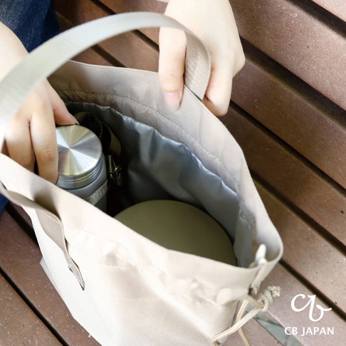 CB JAPAN holms 保冷手提便當袋，米色帆布材質，內部銀色鍍膜，有束口袋設計，裝有銀色保溫瓶和圓形餐盒，由雙手提起。