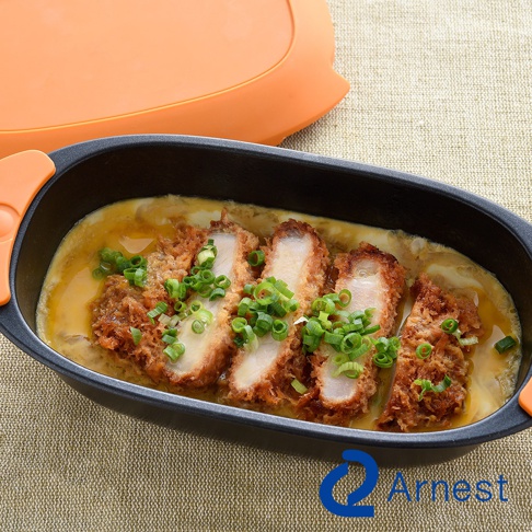 Arnest 多功能快速微波料理器，盛裝著切塊的日式豬排飯，上面灑滿翠綠蔥花，料理器旁擺放著橘色上蓋，整體置於米色織紋背景上。