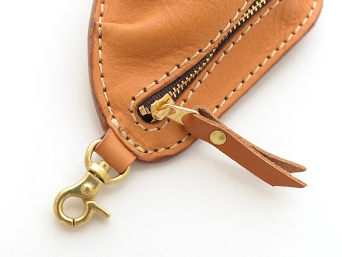 職人手作皮革餃子造型零錢包，採用淺棕色皮革，搭配黃銅色拉鍊及開口環，縫線清晰，皮革帶有自然紋理。