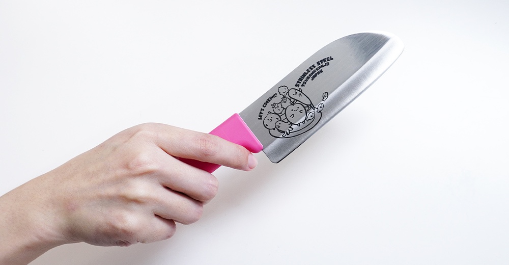 燕三條不鏽鋼兒童學習刀，刀刃長 11.5 公分，手柄為粉紅色，刀面印有卡通蔬菜與魚圖案及「LET'S COOKING! TSUBAMESANJO JAPAN」字樣。