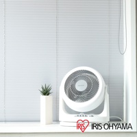 白色IRIS OHYAMA PCF-HM23 空氣循環扇，帶有可調節傾斜角度的底座，扇葉網罩上有品牌標誌。旁邊有一個白色長方形花盆，種植著綠色多肉植物。背景是淺灰色的百葉窗。