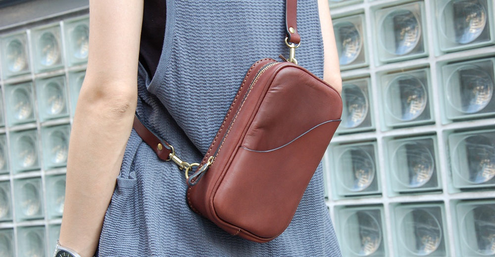 日本人HERZ職人手作皮革兩用直立型斜背包，斜揹於藍灰色連身裙外