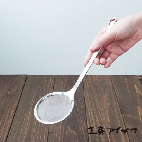 一只手正拿著一把不鏽鋼萬用撈泡勺，勺頭為橢圓形，網孔細密，勺柄為長條形，末端有紅色裝飾。