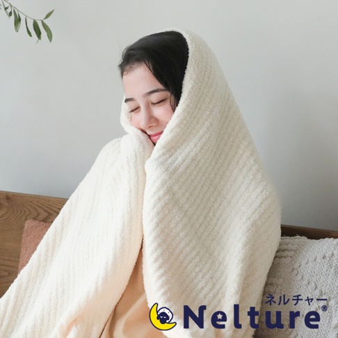一名女子被一條奶油色、帶有紋理的柔暖毛毯包裹，毛毯材質看起來蓬鬆舒適，可見細緻的條紋紋路，營造溫馨居家氛圍。