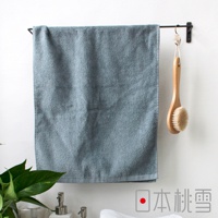 一條藍灰色、觸感細膩的今治柔絨浴巾，懸掛於黑色毛巾架上，旁邊掛著一支木柄沐浴刷。