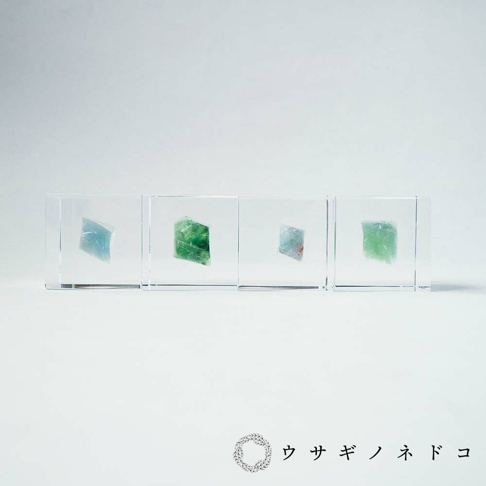 透明立方體內嵌四塊顏色從淺藍到翠綠的礦石，呈現不規則結晶狀。
