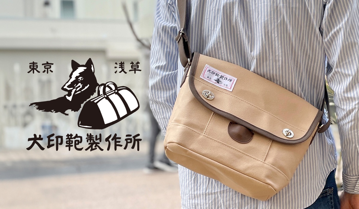 一個男人斜挎著一個卡其色帆布包，包上有一個標籤，背景左側有日文文字和一隻狗與手提包的剪影。