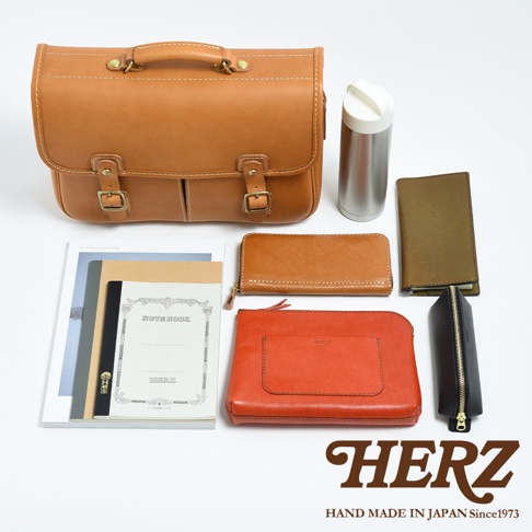 一個棕色皮革的兩用單肩包，配有兩個插扣和提把。周圍散落著一本筆記本、一個長夾、一個橘紅色皮夾、一個綠色長夾、一個黑色筆袋和一個銀色保溫瓶。