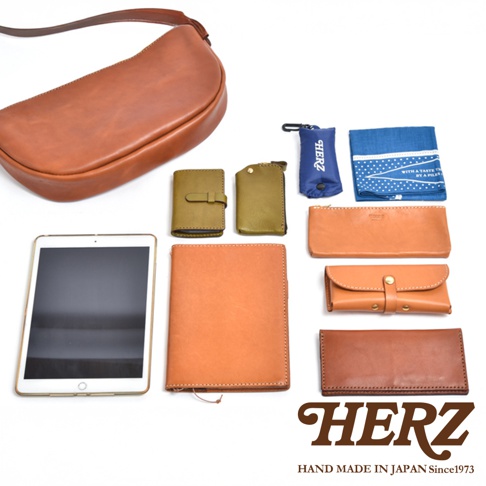 HERZ 職人手作皮革商品，包含馬鞍包、平板電腦、筆記本、錢包、卡夾、零錢包和一條藍色毛巾。
