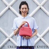 一位女子手持一個珊瑚紅色、荔枝紋皮革的迷你手提包，包身呈半月形，配有雙提把。