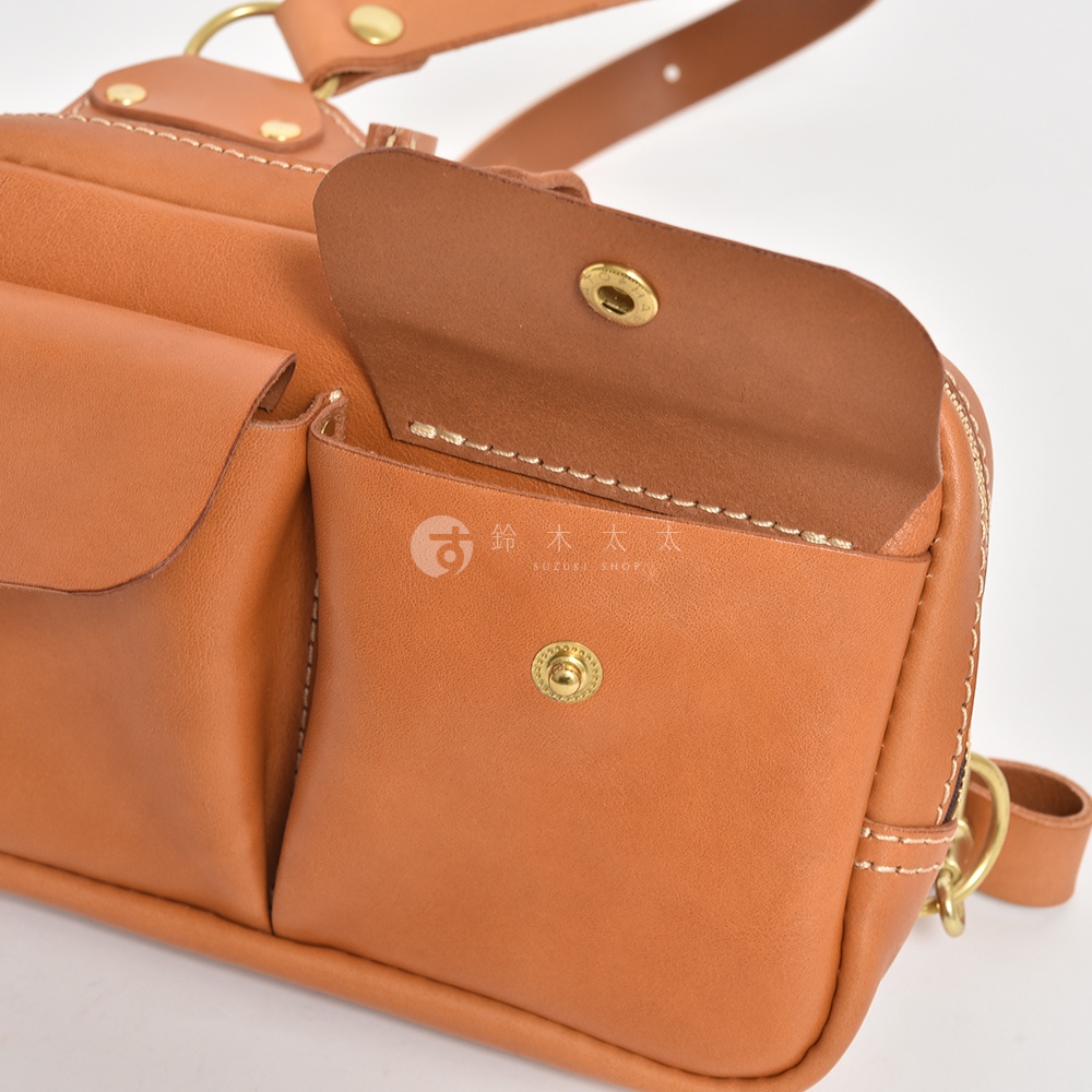 職人手作皮革雙口袋斜背包，展示棕褐色皮革材質，設有兩個前袋，其中一個前袋的蓋子打開，露出金屬按扣。