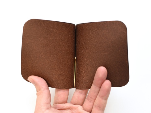 職人手作皮革橫式對折鈔票短夾，採用深棕色皮革，表面帶有自然紋理，由金色金屬夾固定，由手持展示。