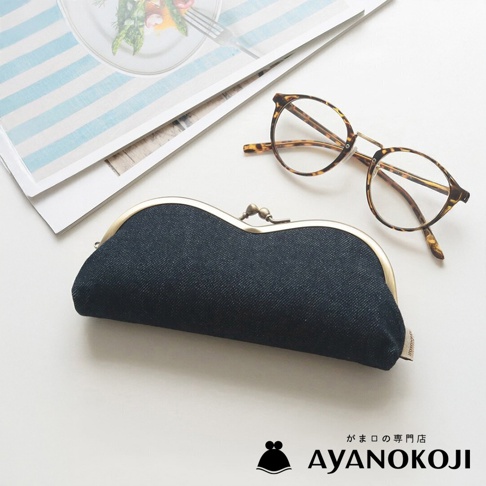 京都職人手作的AYANOKOJI品牌深藍色丹寧布口金眼鏡收納盒，搭配復古玳瑁紋眼鏡，放置於淺色桌面與雜誌上。