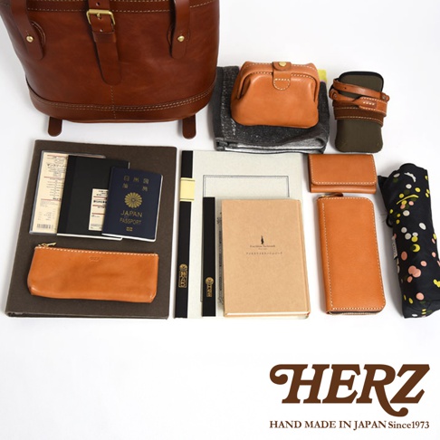 職人手作皮革雙口袋折蓋後背包 R-301，展示多種配件，包括棕色皮革後背包、小錢包、筆袋、護照夾、筆記本、長夾及印有圖案的摺疊傘。