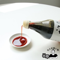 玻璃瓶裝的秘藏醬油，琥珀色醬油正從瓶口傾倒至白色醬油碟中，形成一圈醬油。