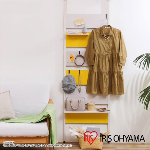 頂天立地木質收納架，白色框架搭配黃色層板，頂部懸掛卡其色連衣裙，側邊掛有灰色帽子、項鍊及裝飾品，下方置有米色手提包、圓形收納盒及裝飾雜誌。