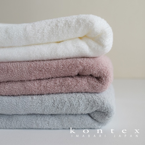 堆疊的浴巾，由上至下分別為白色、粉紅色和淺灰色，質地蓬鬆柔軟。