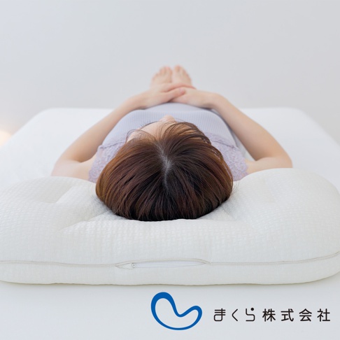 白色良夢調節枕，表面織紋細緻，中央有一拉鍊，枕頭兩側有弧度設計，一位女子正仰躺於枕上，雙手交疊於腹部。