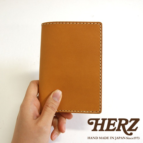 手持一個棕褐色皮革經典護照套，帶有米白色縫線。