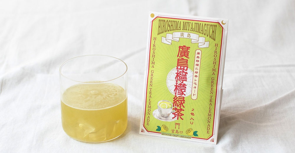 左側放著一杯淡綠色的冰檸檬綠茶，右側則是廣島宮島口檸檬綠茶粉的包裝袋，包裝採淺綠色調設計，印有檸檬插畫與日文產品資訊，呈現出清新自然的沖泡飲品意象。