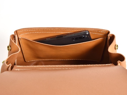 職人手作皮革屋瓦風迷你後背包，展示包包內部，一個棕色皮革隔層中放入一部黑色手機，縫線清晰，整體為淺棕色皮革。