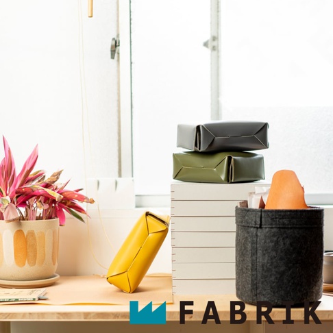 FABRIK 品牌的灰色與橄欖綠色皮革收納盒堆疊擺放，旁邊有一個黃色條狀小物，背景是明亮的窗戶。