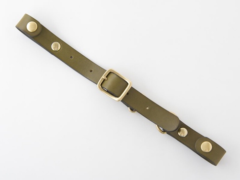 橄欖綠皮革製成的背包減壓胸前扣帶，配有黃銅色金屬扣環、鉚釘和 D 型環。