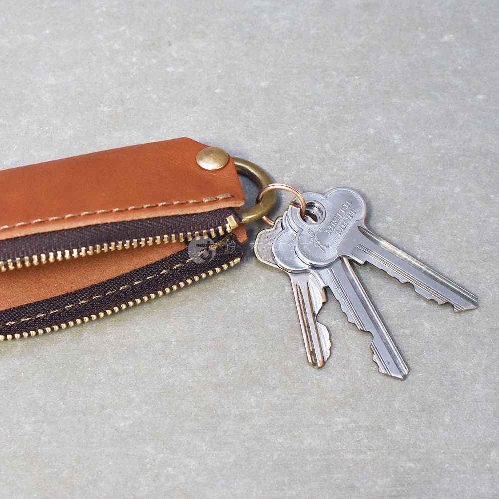 職人手作皮革Organ拉鍊鑰匙包，採用棕色皮革和深棕色拉鍊，搭配黃銅色五金配件，掛有三把銀色鑰匙。