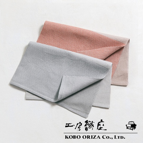兩條顏色不同的鬆餅紋拭巾，一條是粉紅色，另一條是灰色，疊放在一起，下方有 KOBO ORIZA Co., LTD. 的品牌標誌。