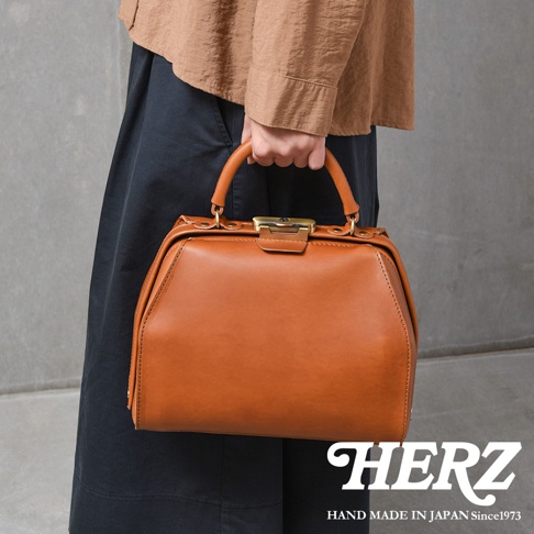 職人手作的棕色皮革兩用口金手提包，具有經典的醫生包造型，頂部配有金色金屬開合扣和提把。