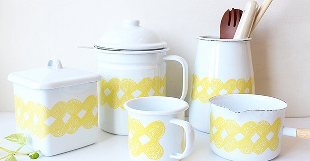 白色琺瑯馬克杯，帶有黃色編織圖案裝飾，杯緣黑色滾邊。