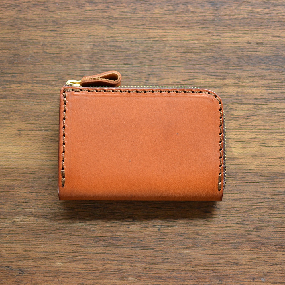 一個棕褐色皮質的拉鍊短夾，頂部有金色拉鍊和皮革拉環，邊緣有縫線，放置在木紋桌面上。