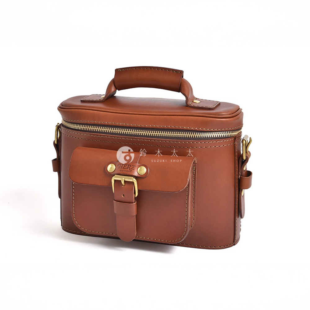 HERZ 品牌復古棕色皮革相機包，配有翻蓋口袋和黃銅扣環，頂部有手柄和拉鍊開口