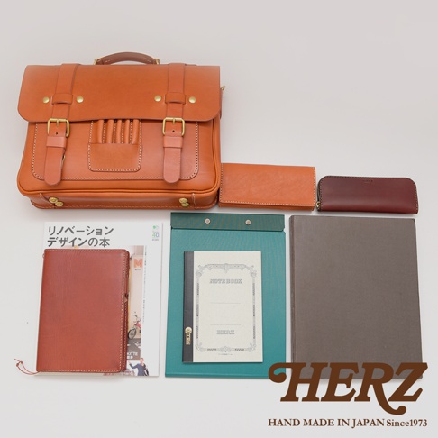 職人手作皮革傳統歐風三用學生包，顏色為棕色，搭配金色金屬釦件，材質為皮革。另有橘色和深紅色皮革長夾、筆記本和文件夾。