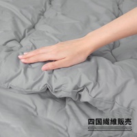 一張圖片，一只手放在灰色被子中間，被子表面有皺褶，右下角有日文文字「四國纖維販売」。