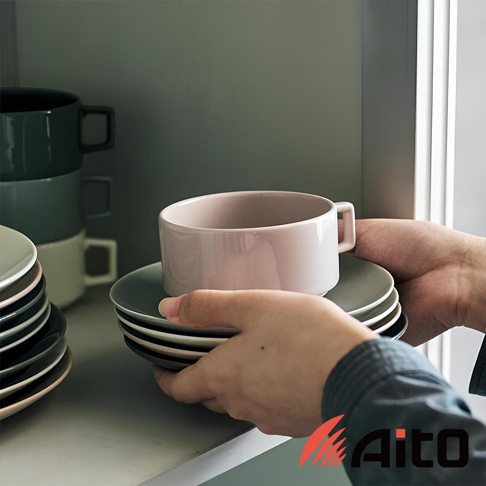 一隻手正在疊放著一系列粉色、灰色和深灰色的圓形陶瓷餐盤，盤子上放著一個粉色陶瓷杯。